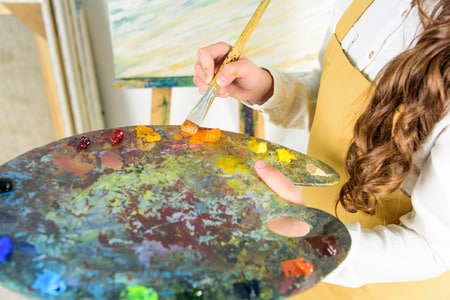 child holding an oil paint palette and brush